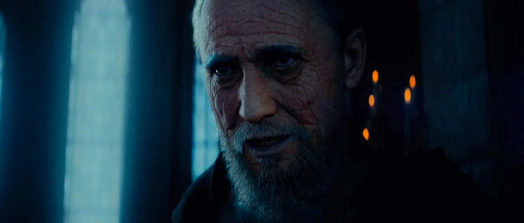 A close portrait of an older bearded man in cold blue light.