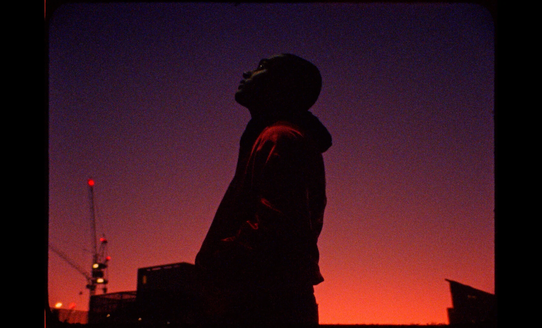 A silhouetted figure stands against a red-purple dusk sky.