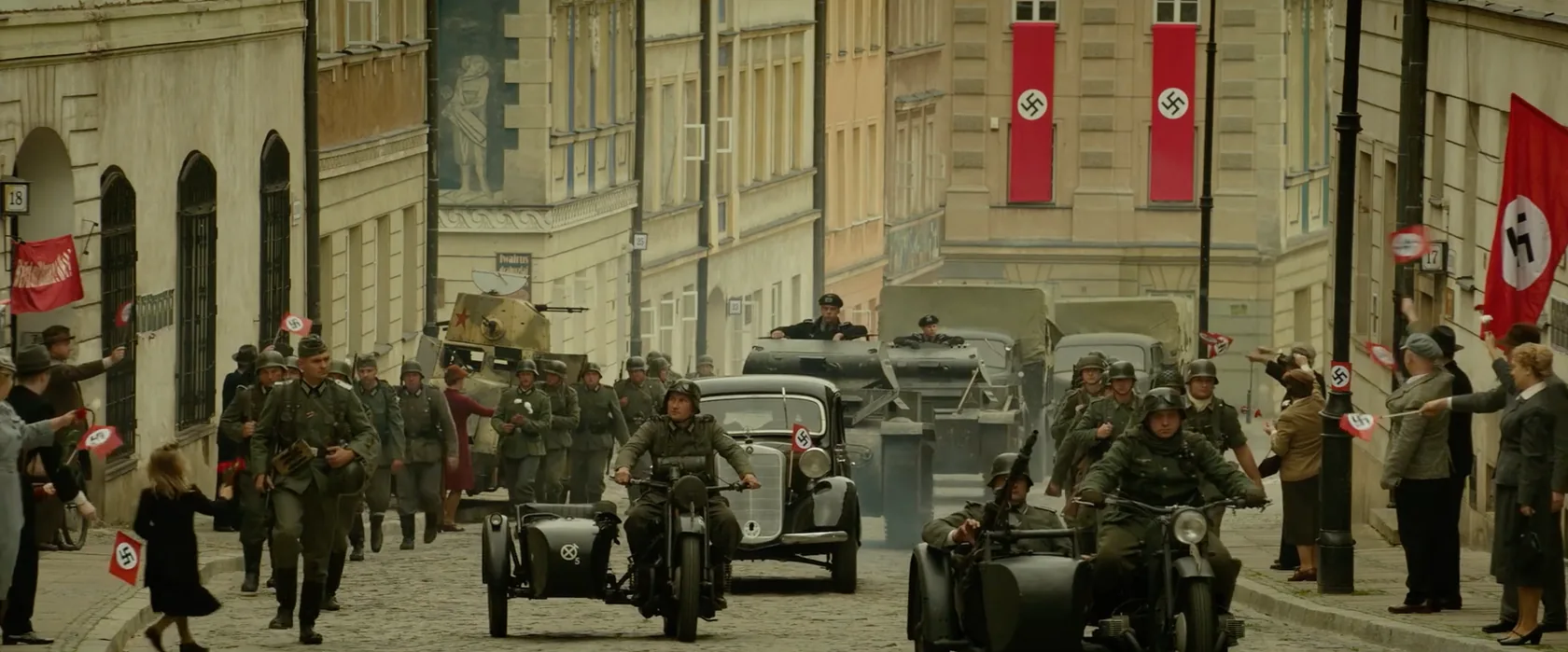 An occupied city street with soldiers, vehicles, and red banners.