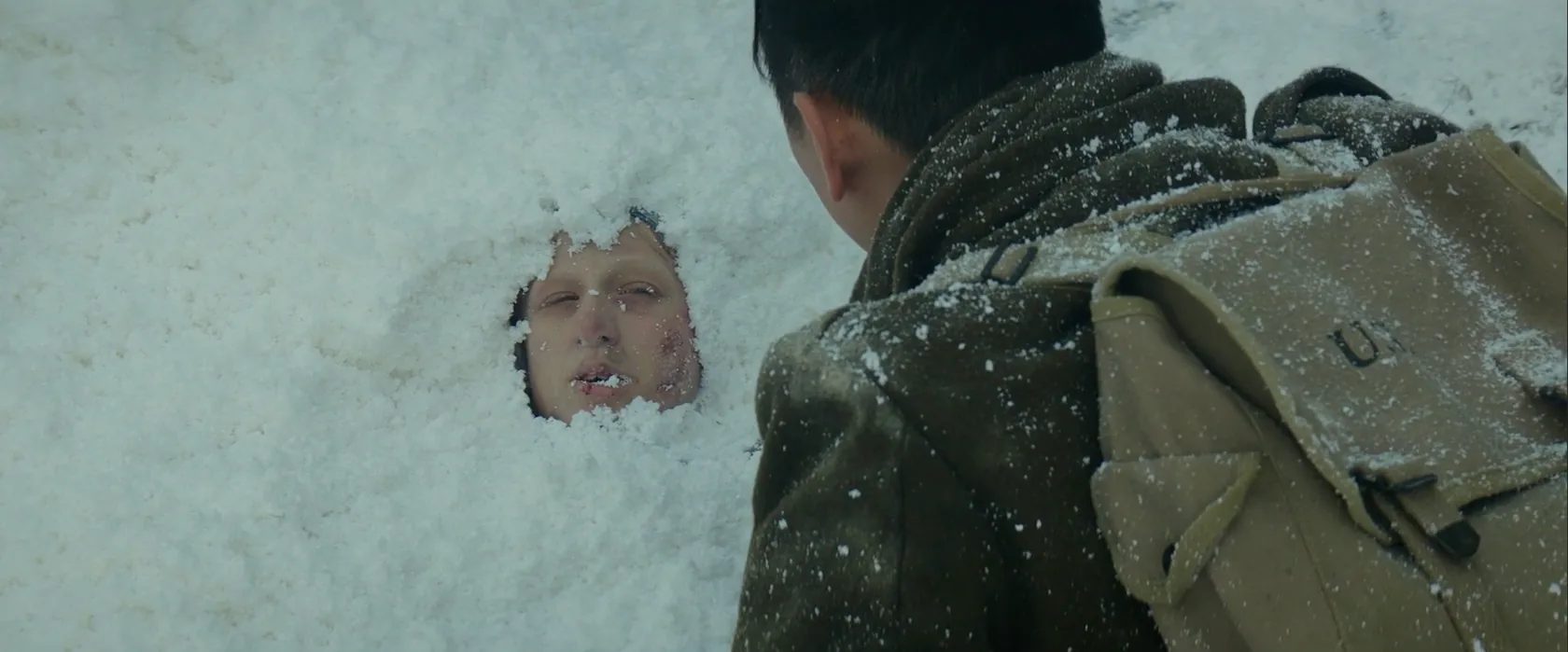 A face emerging from deep snow as a traveler looks on.