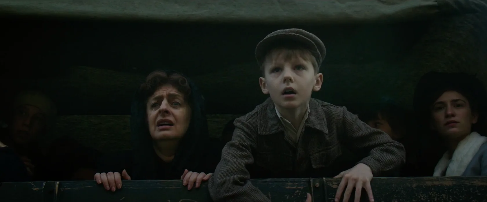 A child and passengers look out from a dark train carriage.