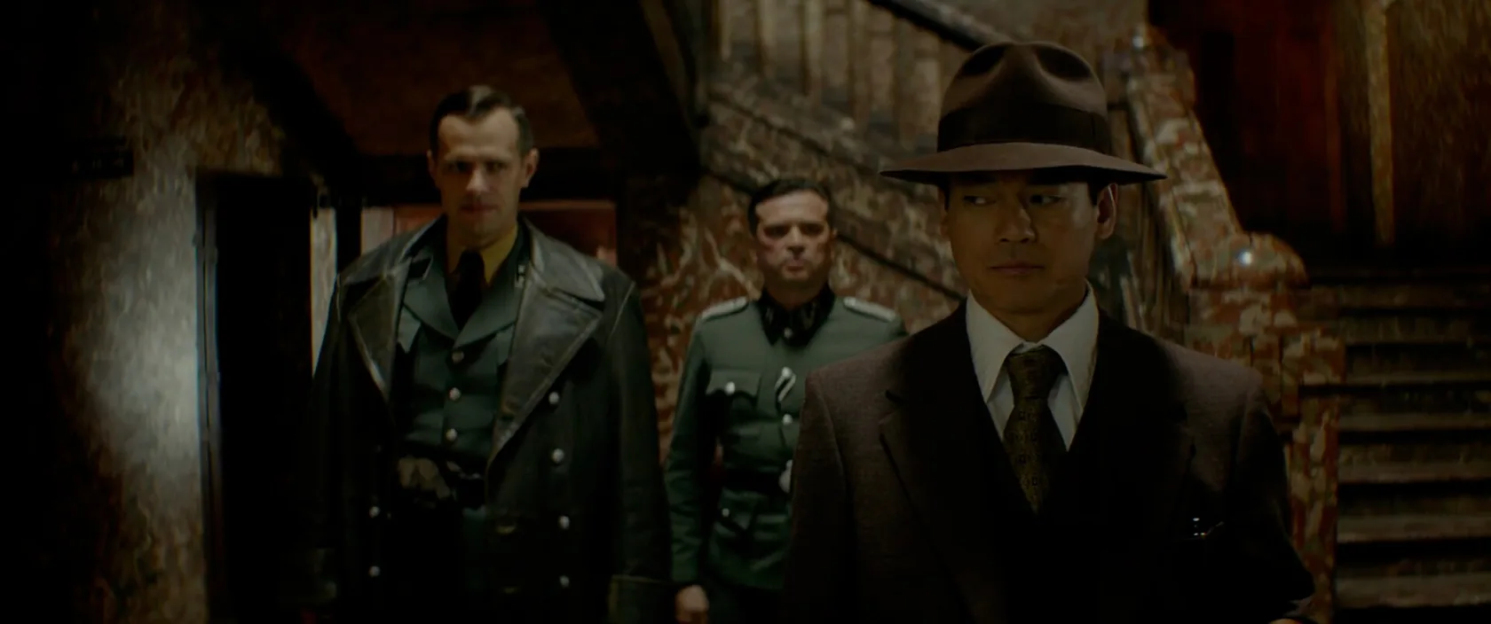 Three men in period clothing move through a dim staircase.